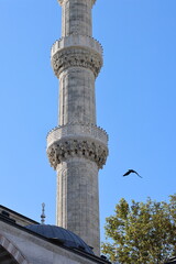 A close-up view of a tall, white minaret with intricate stone detailing and a pointed spire, set...