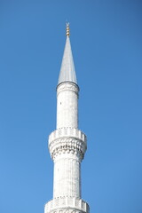 A close-up view of a tall, white minaret with intricate stone detailing and a pointed spire, set...