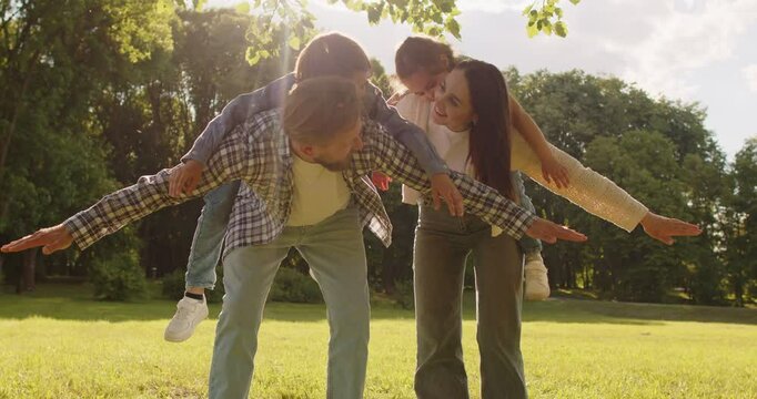 Happy playful mother and father giving piggy back to their children in park, having fun during weekend, breathing fresh air and enjoying sunset. Family, leisure, parenthood, entertainment