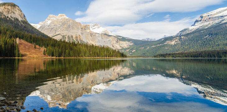 Stunning view of Emerald Lake in Yoho National Park with snow-capped mountains and pine coniferous forests with with scattered rocks along peaceful shoreline in Alberta, Canada - Powered by Adobe