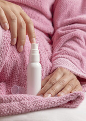 Closeup of young woman in pink bathrobe holding white spray cosmetic bottle, girly mockup