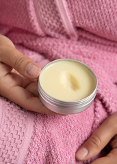 Closeup of young woman in pink bathrobe with opened body butter jar in hand. Bodycare concept