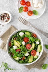Fresh salad with arugula, mozzarella, tomatoes and avocado in a bowl. Healthy vegetarian dish.