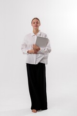 Young woman stands confidently holding a laptop in a bright studio setting during a creative work...