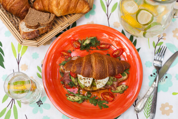 Homemade croissant sandwich with avocado, poached egg, bacon, arugula, and cherry tomatoes. A stylish brunch with a child enjoying the meal