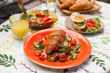 Homemade croissant sandwich with avocado, poached egg, bacon, arugula, and cherry tomatoes. A stylish brunch with a child enjoying the meal