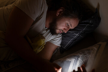 Man lying in bed checking smartphone at night
