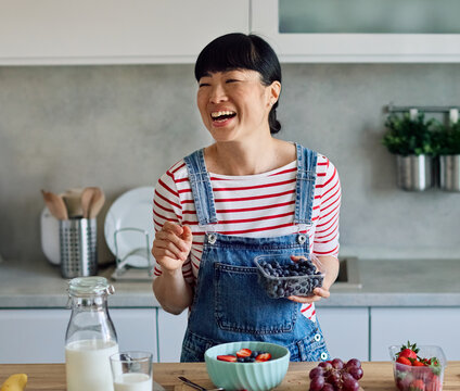 Portrait of a healthy young asian woman enjoying delicious fruit and cereal salad breakfast bowl at home