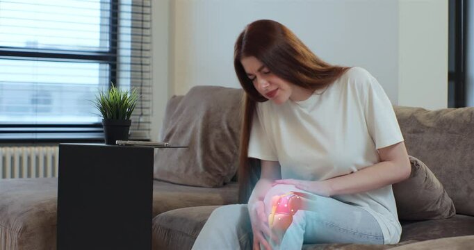 3d augmented reality animation joint and knee pain. Young woman touching her knee feel pain and doing massage sitting on couch at home. People health care problem.