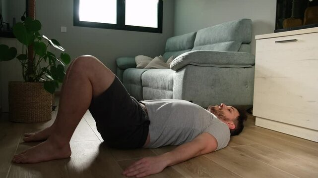 Man is training his glutes and core muscles by performing a bridge exercise on the floor of his living room