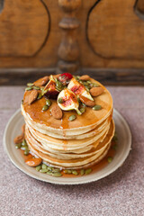 Stack of pancakes with fresh fig, strawberries, maple syrup, and crunchy toppings. A warm, comforting outdoor breakfast with orange juice and coffee