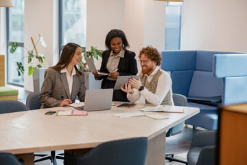 In a modern stylish office, three professionals engage in a collaborative discussion to share...
