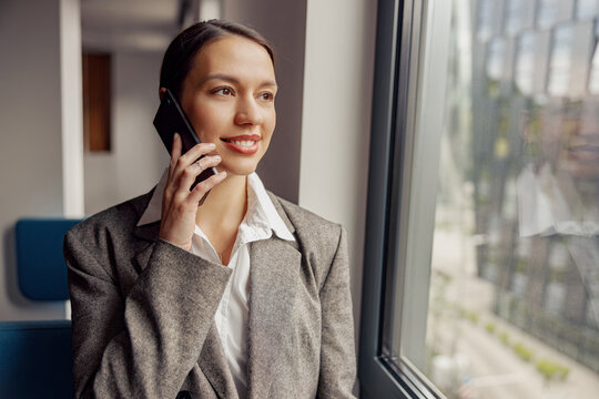 A successful businesswoman is on a crucial phone call while gazing out a large window in her modern office
