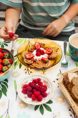 Heart-shaped waffles topped with berries and whipped cream. A cheerful brunch moment with a child enjoying the treat