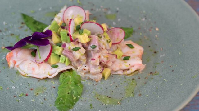 Delightful ceviche made with fresh dorade and shrimp, complemented by avocado and radish, garnished with an edible flower on a serene green plate.