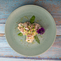 Delightful ceviche made with fresh dorade and shrimp, complemented by avocado and radish, garnished with an edible flower on a serene green plate.