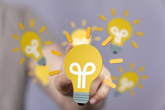 Person's fingertip touches a glowing lightbulb, symbolizing innovation and ideas.