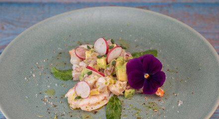 Delightful ceviche made with fresh dorade and shrimp, complemented by avocado and radish, garnished with an edible flower on a serene green plate.