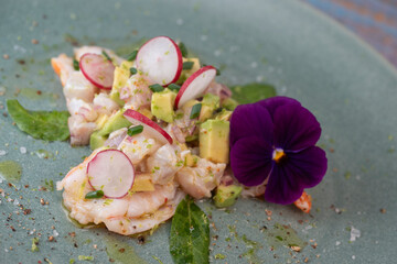 Delightful ceviche made with fresh dorade and shrimp, complemented by avocado and radish, garnished with an edible flower on a serene green plate.