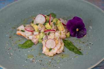 Delightful ceviche made with fresh dorade and shrimp, complemented by avocado and radish, garnished with an edible flower on a serene green plate.