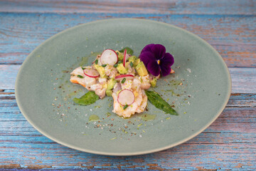 Delightful ceviche made with fresh dorade and shrimp, complemented by avocado and radish, garnished with an edible flower on a serene green plate.