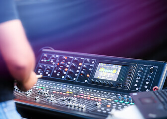 Professional sound engineer adjusting a digital audio mixing console during a live event. Modern...