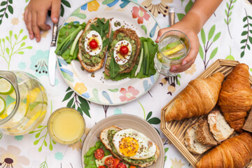 Rustic avocado toasts on oval bread served for a cozy family brunch with orange juice, croissants,...