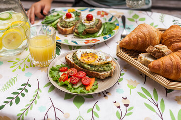 Rustic avocado toasts on oval bread served for a cozy family brunch with orange juice, croissants,...