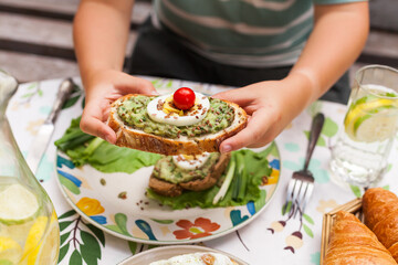 Rustic avocado toasts on oval bread served for a cozy family brunch with orange juice, croissants,...