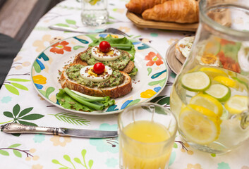Rustic avocado toasts on oval bread served for a cozy family brunch with orange juice, croissants,...