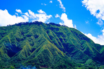 Panoramic view of green landscape with mountains, blue sky and white clouds from Selong Hill, Sembalun, Lombok, West Nusa Tenggara, Indonesia.