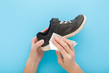 Young adult woman hands holding dry white paper napkin and dark black kid sport shoe on light blue...