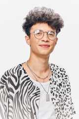 Young man smiling with curly hair and glasses wearing a mixed animal print shirt and layered silver...