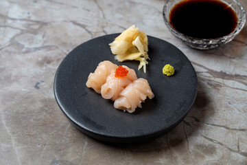 Delicate sushi pieces rest elegantly on a round black plate, accompanied by wasabi, pickled ginger,...