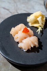 A beautifully arranged dish features delicate sushi with translucent seafood topped with a pop of orange roe, accompanied by slices of fresh ginger, creating an inviting culinary experience