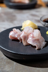 Delicate slices of sashimi are elegantly arranged on a sleek black plate, accompanied by wasabi and soy sauce in a contemporary restaurant