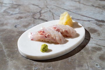 Delicate sushi pieces rest elegantly on a smooth white plate, accompanied by wasabi and pickled...