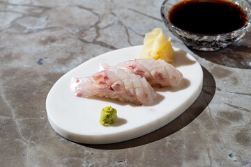 On a sleek marble surface, two pieces of sushi present an artistic arrangement of fresh fish. Accompanied by dollops of wasabi and pickled ginger, soy sauce awaits for dipping