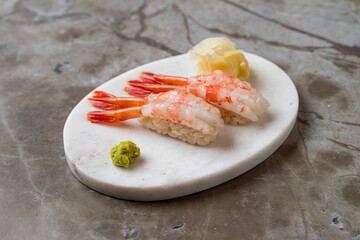 Delicate shrimp nigiri sits beautifully on a smooth, oval platter, accompanied by bright green wasabi and pickled ginger. The calming atmosphere enhances the culinary artistry displayed