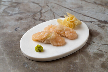 Delicate sushi sits artfully arranged on a modern white plate, featuring translucent fish atop vinegared rice. Accompanied by wasabi and ginger, the scene exudes elegance and culinary artistry