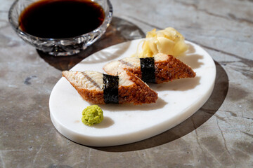 Crispy sushi delicately garnished with wasabi and pickled ginger sits on a smooth marble plate accompanied by a small bowl of dipping sauce. The elegant dining atmosphere enhances the experience