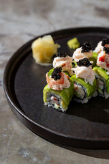 Gourmet sushi rolls featuring fresh crabmeat, smooth avocado, and luxurious caviar are served on a sleek black plate, complemented by pickled ginger, creating a culinary masterpiece