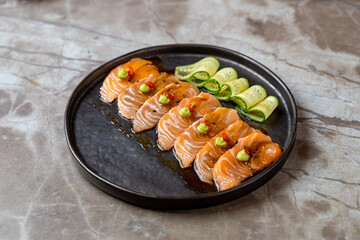 Delicate slices of fresh salmon are artfully arranged on a sleek black plate, accompanied by thinly sliced cucumbers and vibrant garnishes, showcasing culinary artistry at its finest
