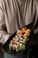 A skilled chef presents an artfully arranged sushi platter featuring various rolls and fresh seafood, inviting diners to indulge in culinary excellence during dinner