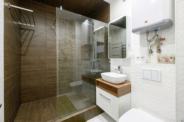 modern bathroom with a glass-enclosed shower, pebble accent wall, white sink on a wooden cabinet, and white textured tiles. A mirror and water heater are also visible