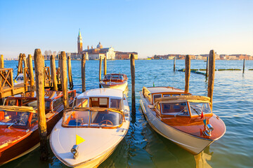 Wooden water taxis docked on a calm Venetian canal at sunset, with San Giorgio Maggiore in the...