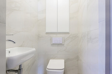 minimalist bathroom with white marble tiles, a white sink, toilet, and cabinet. Clean, bright, and modern