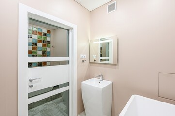 Modern bathroom featuring a unique tiled wall seen through a semi-frosted door, complemented by a sleek sink and lighted mirror