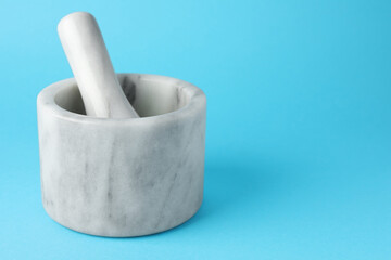 Marble mortar and pestle on light blue background, closeup. Space for text