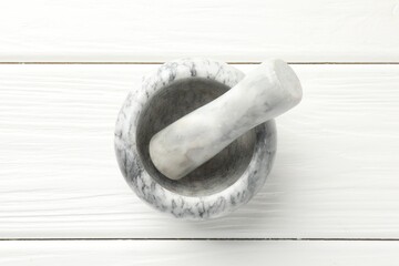 Marble mortar and pestle on white wooden table, top view